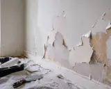 Ściana łuszczy się, a pod nią widać starą farbę. Przygotowania do malowania: kuweta z wałkiem i szpachelka. Co zrobić, gdy farba nie kryje?